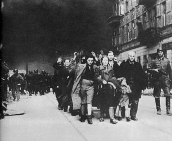 Jews are marched through the streets of the Warsaw ghetto as it burns.